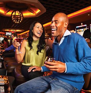 couple with drinks laughing at a slot machine